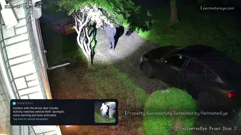 The searchlight following the person past the tree along the driveway, with Property Successfully Defended by PerimeterEye on screen